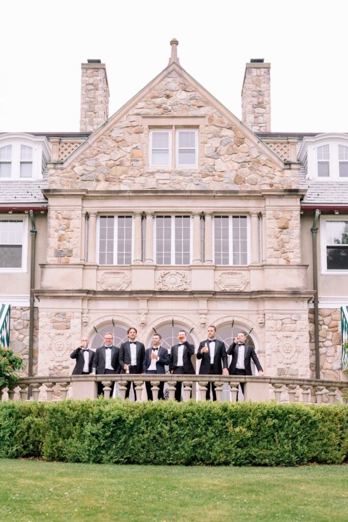 A groom and his wedding party toasting in front of a stone building wedding venue