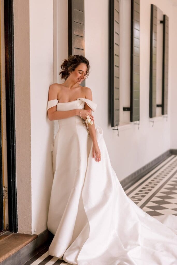 Beautiful young bride in her dress leaning against the wall smiling