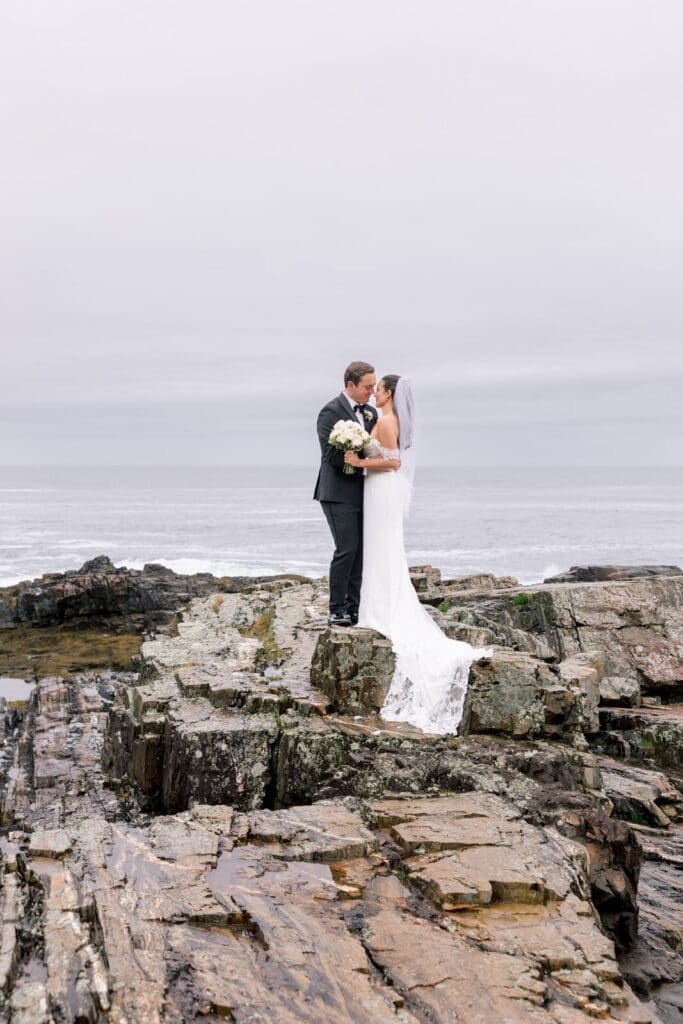 A bride and groom posing on cliffside rocks on their wedding day in New England